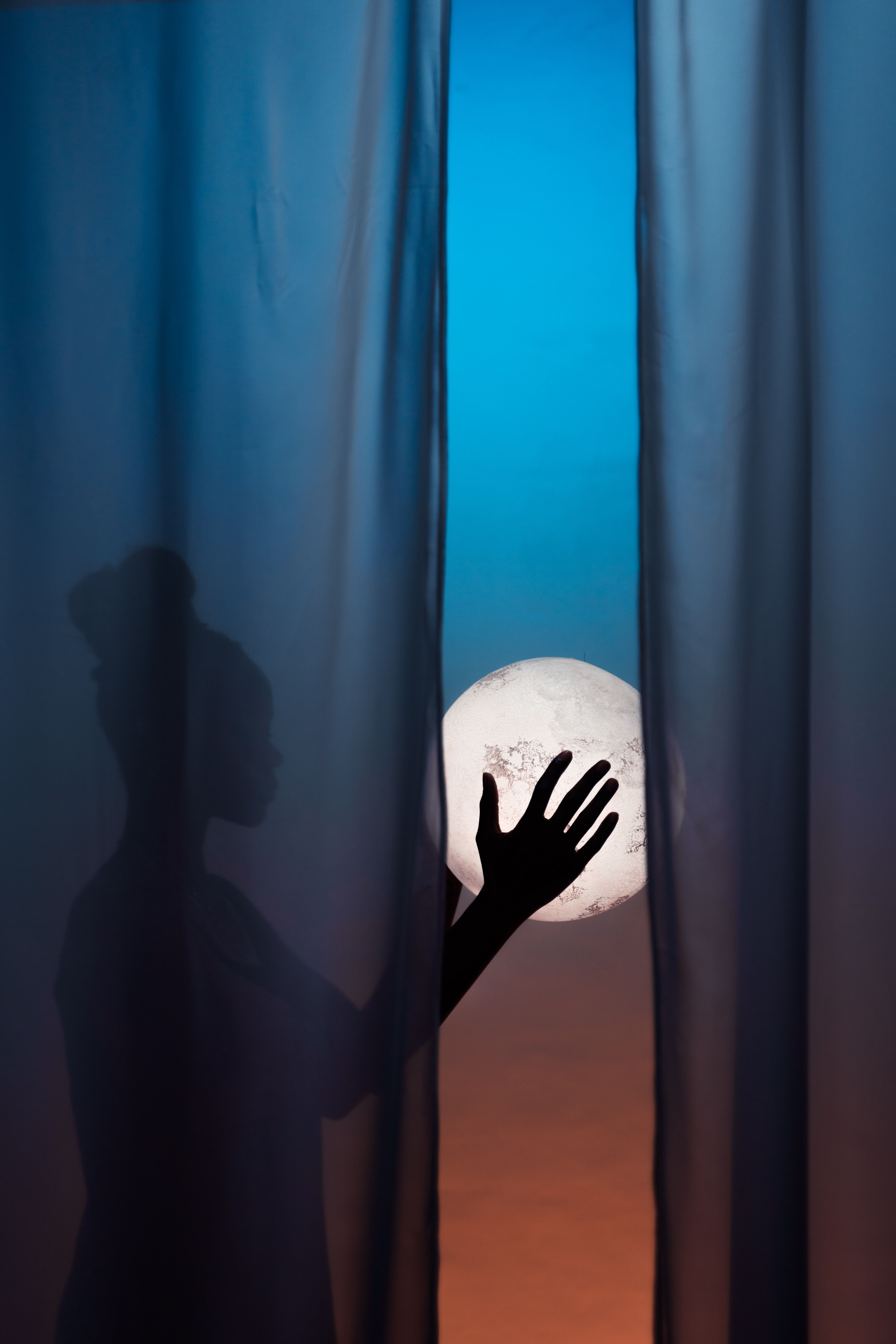 Mujer con la luna al fondo tras una ventana