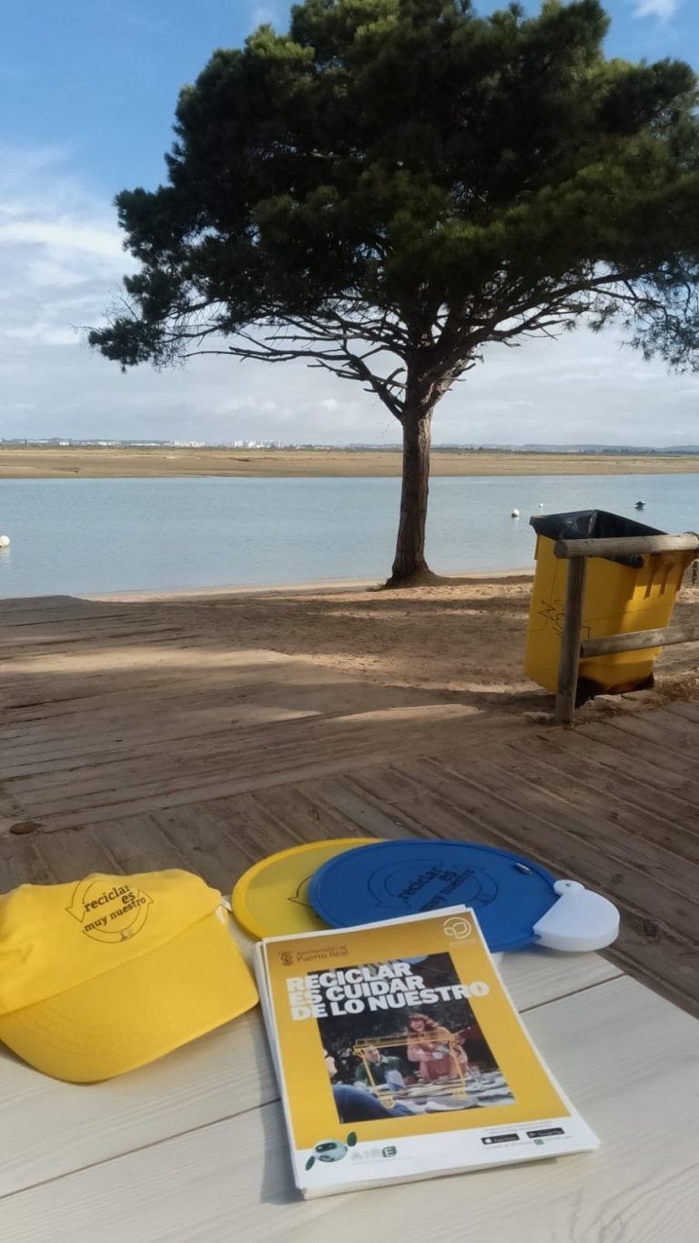 Contenedor amarillo y puesto de información de reciclaje frente a una playa de Puerto Real, Cádiz