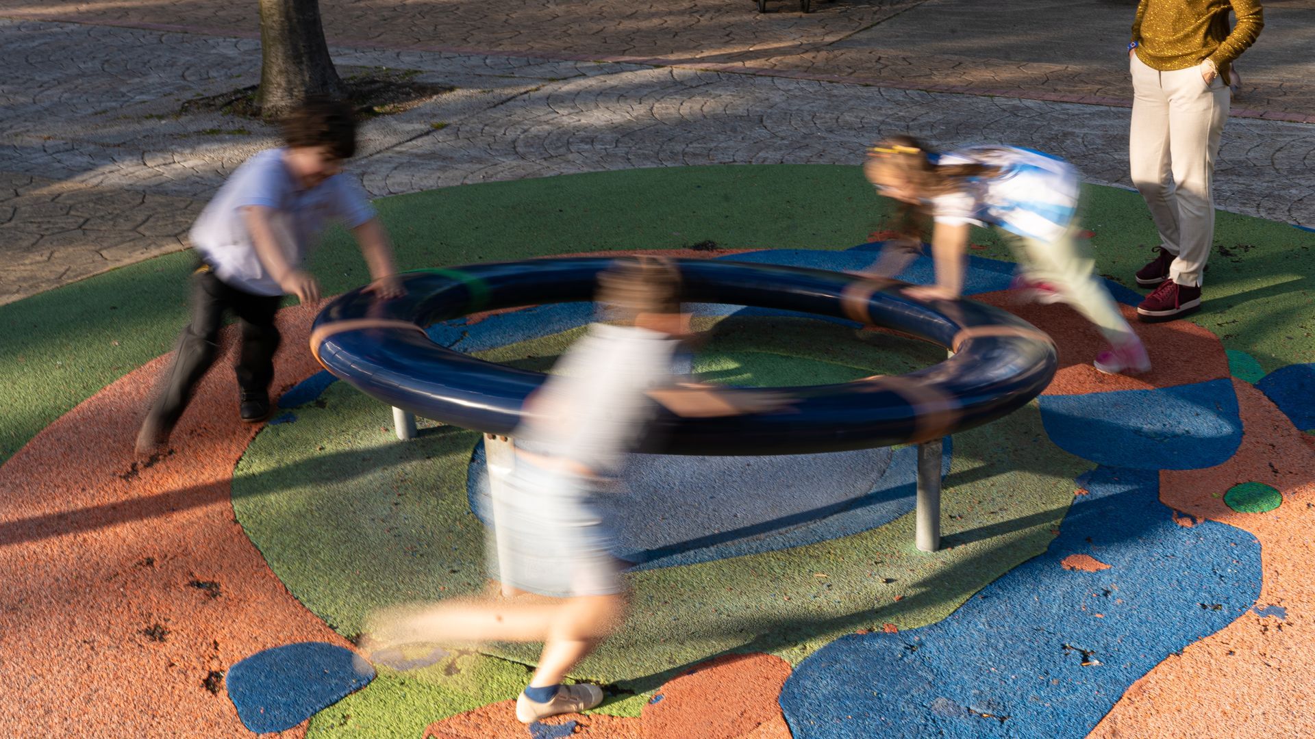 Niños juegan en un parque infantil de Gijón con el pavimento de caucho visiblemente desgastado, el pasado año